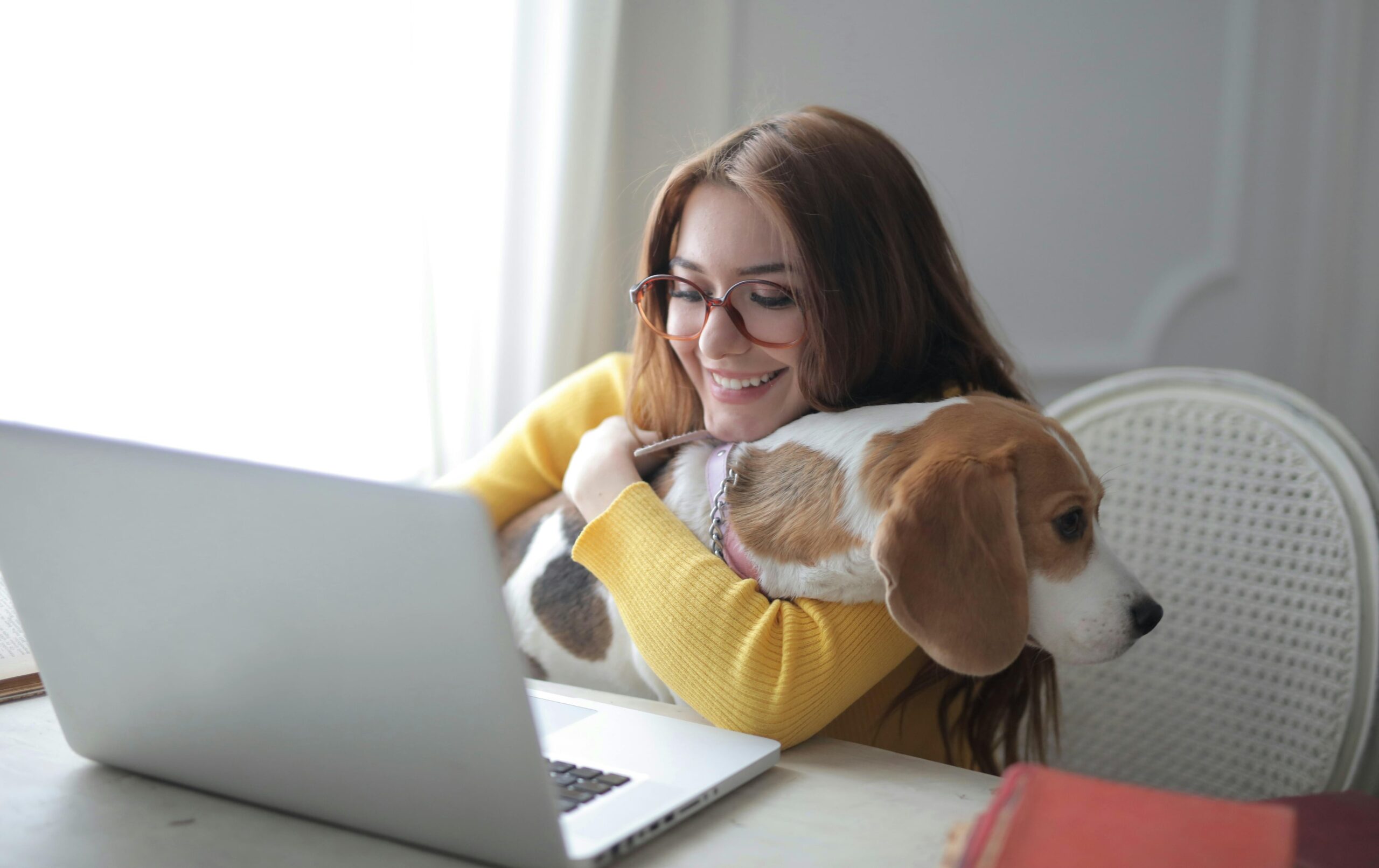 A young woman in a yellow sweater, holding a dog while on her laptop, having a legal document drafted during a video call