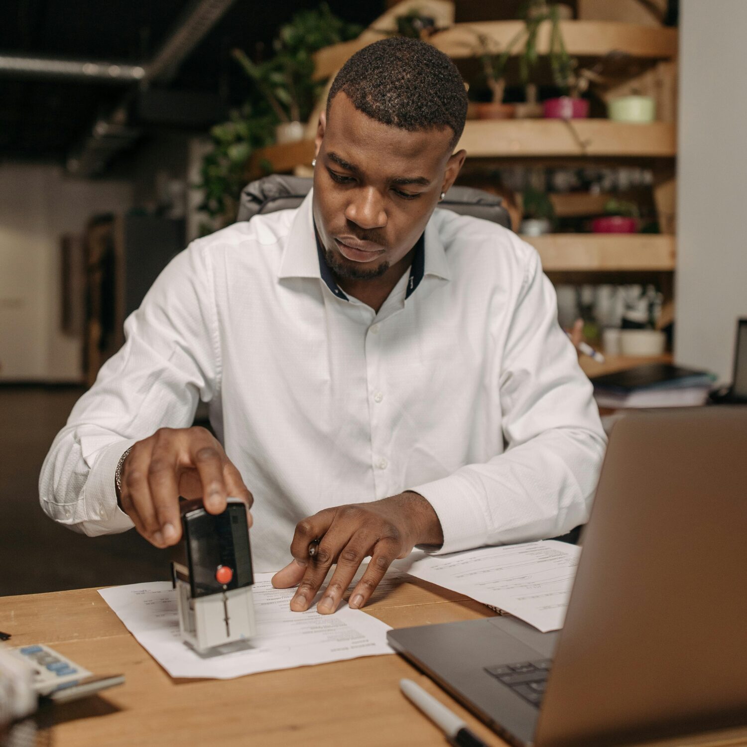 Young Black man in a white button-up shirt, stamping paperwork.