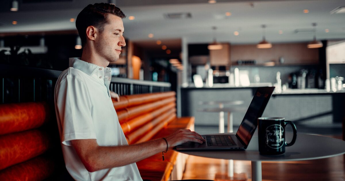 Young Caucasian man sitting in a coffee shop, on his laptop.