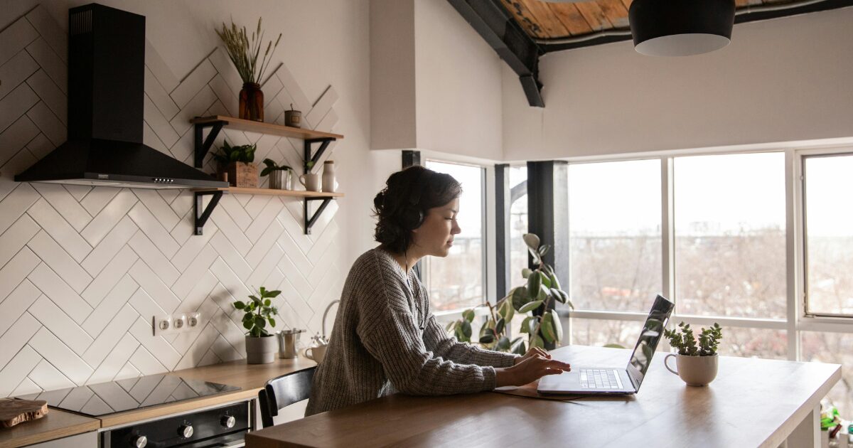 Young Caucasian woman with short brown hair, on her laptop at wood table, in a modern kitchen