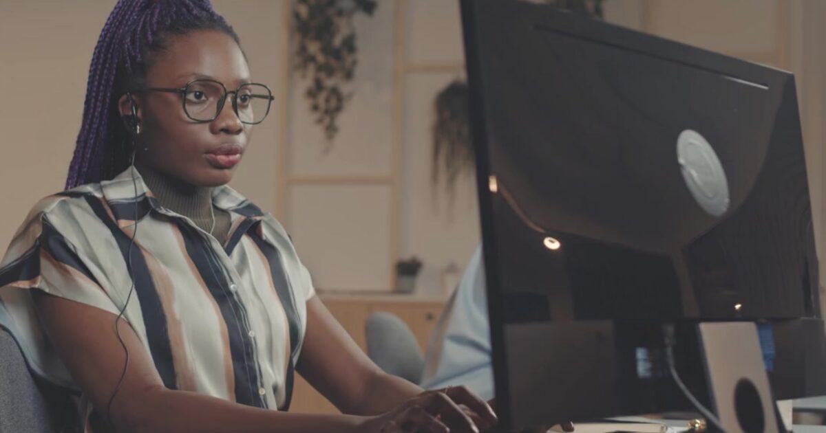 An adult Black woman with her hair up, wearing glasses, working on a terminal.