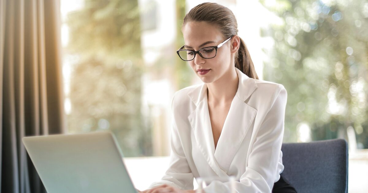 Young Caucasian woman typing on a laptop typing in a white blouse.